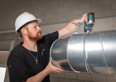 Monteur met helm en boormachine die luchtkanalen aan het monteren is