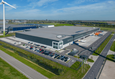 Groot distributiecentrum met daaromheen gras en een windmolen